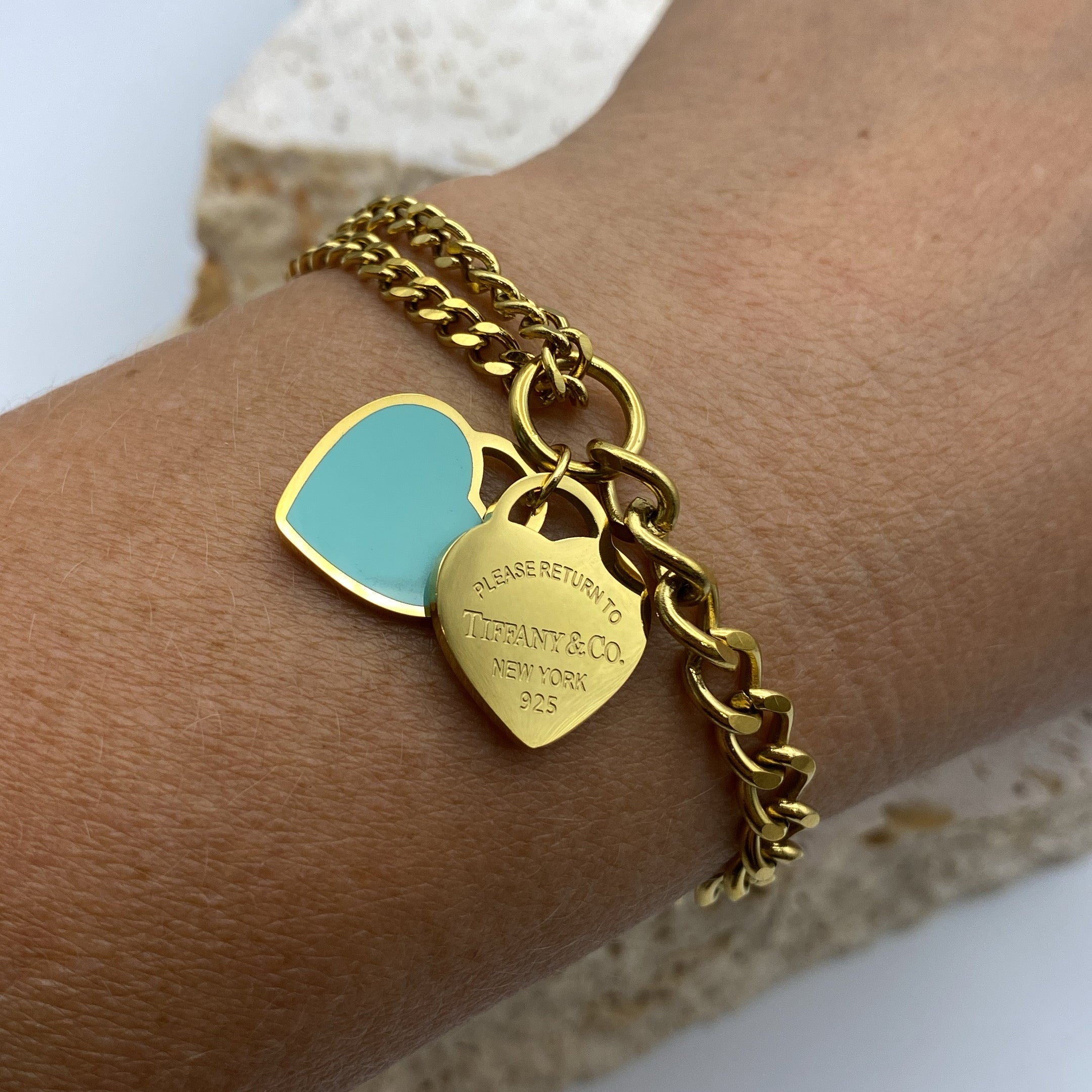 Gold chain bracelet with heart-shaped tags on a wrist against a neutral background